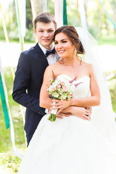 Bröllopsparet kramas, bruden håller en bukett blommor, brudgummen omfamna henne — Stockfoto