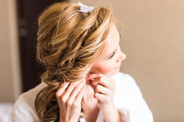 Elegante novia rubia poniéndose los pendientes de cerca, preparándose para la boda —  Fotos de Stock