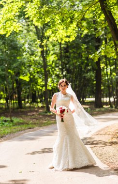 Güzel gelin bir parkta açık havada düğün buketi ile.