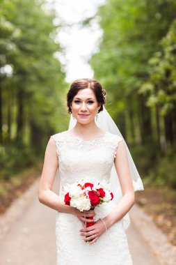 Güzel gelin bir parkta açık havada düğün buketi ile.