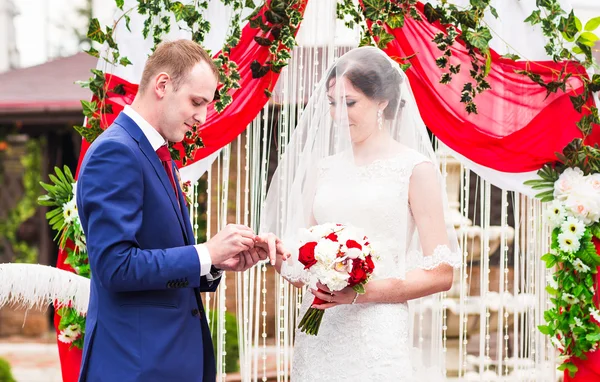 Pareja en anillos de intercambio de atuendos de boda con arco sobre fondo — Foto de Stock