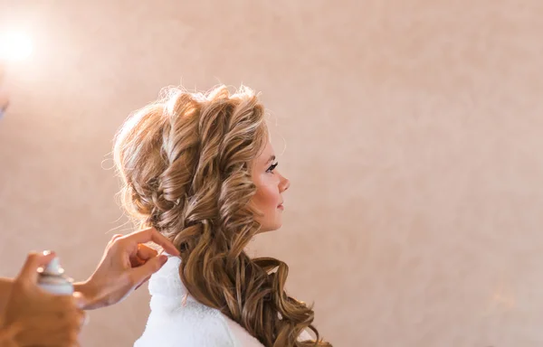 Artista de maquiagem de casamento fazendo uma maquiagem para a noiva. Menina modelo sexy bonita dentro de casa. Mulher loira beleza com cabelo encaracolado. Close-up mãos perto do rosto — Fotografia de Stock