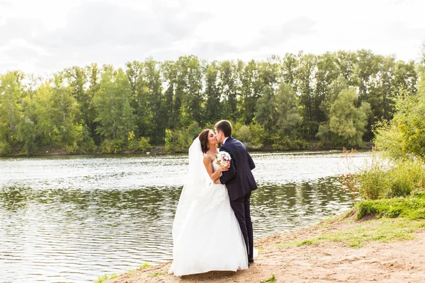 Couple de mariage debout et baisers près du lac . — Photo