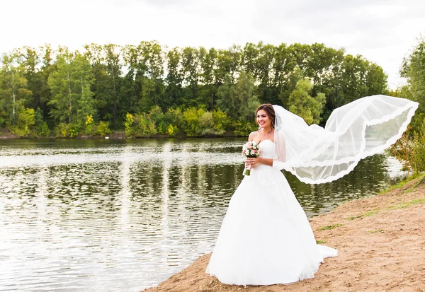 Noiva em um vestido branco com buquê de casamento no lago — Fotografia de Stock