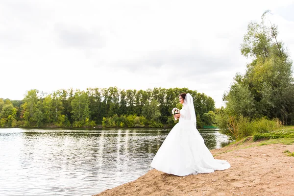 Наречена в білій сукні з весільним букетом на озері — стокове фото