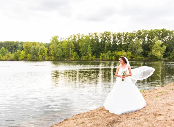 Noiva em um vestido branco com buquê de casamento no lago — Fotografia de Stock