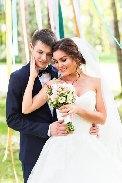 Casamento casal abraçando, noiva segurando um buquê de flores, o noivo abraçando-a — Fotografia de Stock