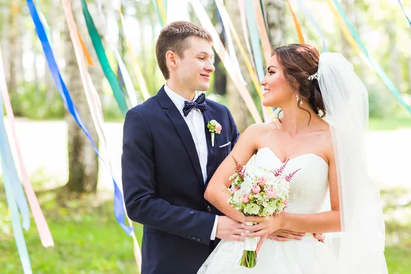 Ζευγάρι του γάμου αγκάλιασμα, κρατώντας ένα μπουκέτο λουλούδια, ο γαμπρός αγκαλιάζοντάς την νύφη — Φωτογραφία Αρχείου