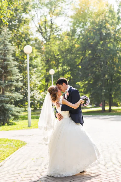 Couple de mariage câlin, la mariée tenant un bouquet de fleurs, marié embrassant son — Photo