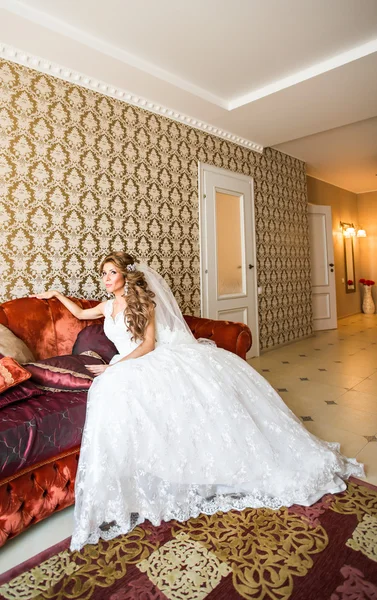 Schöne junge Braut mit einem Brautstrauß auf dem Sofa sitzend. — Stockfoto