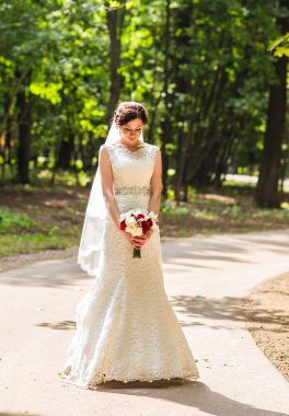 Güzel gelin bir parkta açık havada düğün buketi ile.
