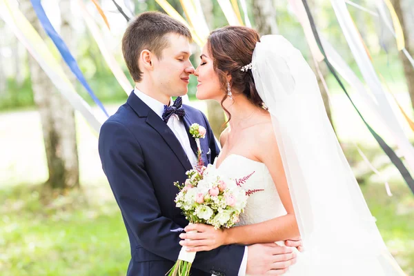 Casamento casal beijando, noiva segurando um buquê de flores, noivo abraçando-a — Fotografia de Stock