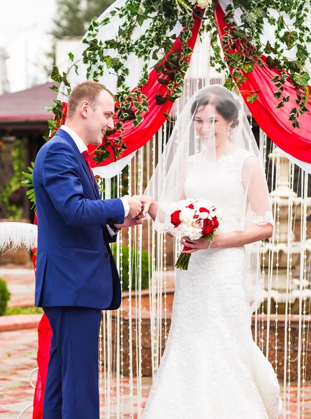 Paar in Hochzeitskleidung Tauschringe mit Bogen auf dem Hintergrund — Stockfoto