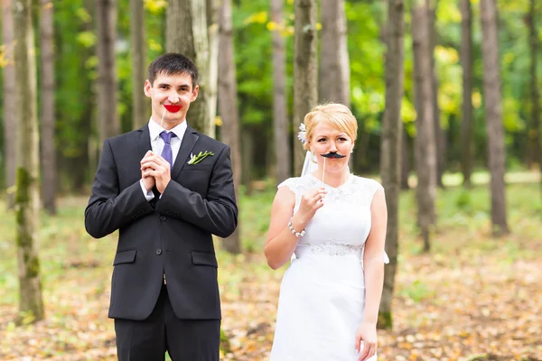 Aprilscherz. Hochzeitspaar posiert mit Stocklippen, Maske. — Stockfoto