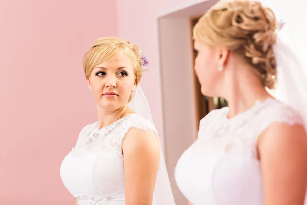 Mooie bruid meisje met kapsel en lichte make-up kijkt in de spiegel — Stockfoto