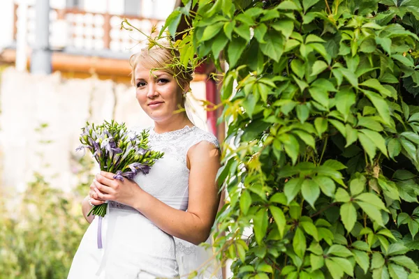 Młode panny młodej w sukni ślubnej trzymając bukiet, na zewnątrz — Zdjęcie stockowe