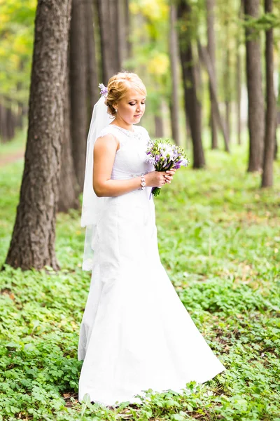 Mladá nevěsta ve svatebních šatech drží kytici, venku — Stock fotografie