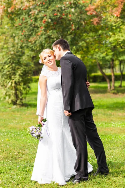 Mooie bruidspaar in park. zij kussen en omhelzen elkaar — Stockfoto