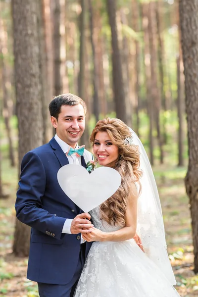 Happy brudgummen och bruden i en park med tecken som hjärta — Stockfoto