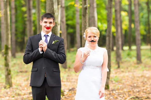 Πρωταπριλιά ημέρα. Γαμήλιο ζεύγος ποζάρει με χείλη ραβδί, μάσκα. — Φωτογραφία Αρχείου