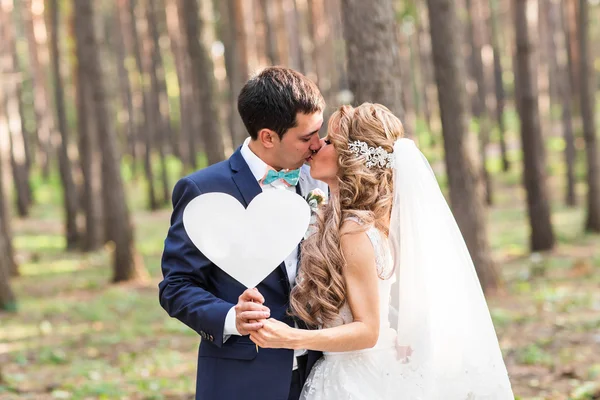 Gelukkige bruid en bruidegom in een park met teken als hart — Stockfoto