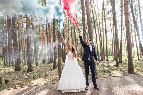 Los novios con bombas de humo en el fondo de los árboles —  Fotos de Stock