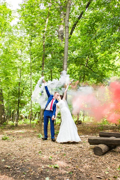 A noiva e o noivo com bombas de fumaça no fundo das árvores — Fotografia de Stock