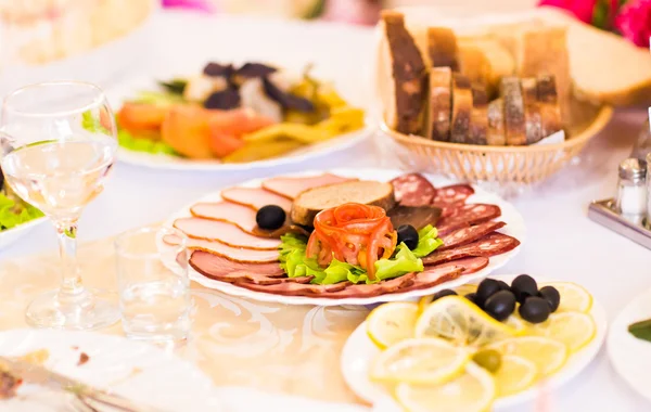 Schotel van gesneden ham, salami en gerookte vlees met plantaardige decoratie op feestelijke tafel — Stockfoto