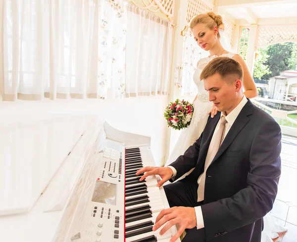 Pareja de boda tocando un piano en la habitación — Foto de Stock