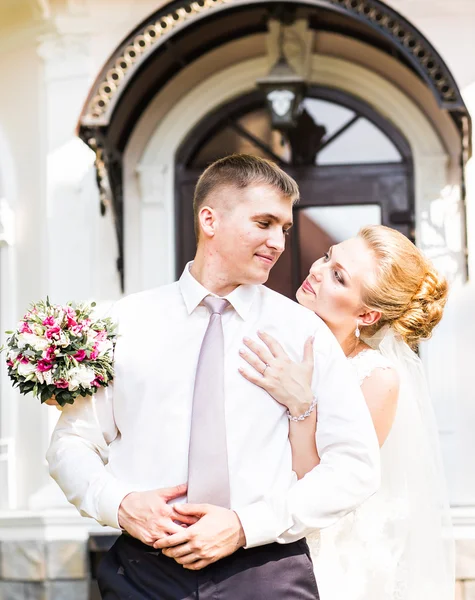 Bruidspaar knuffelen, bruid houden een boeket van bloemen, de bruidegom omarmen haar — Stockfoto
