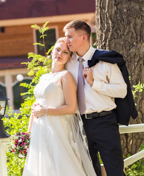 Couple de mariage câlin, mariée tenant un bouquet de fleurs, le marié l'embrassant — Photo