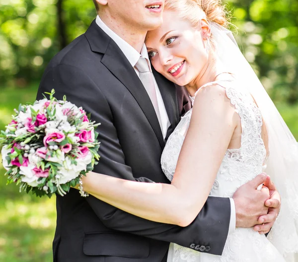 Casamento casal abraçando, noiva segurando um buquê de flores, o noivo abraçando-a — Fotografia de Stock