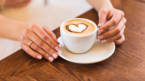 Mulher segurando xícara quente de café, com forma de coração — Fotografia de Stock