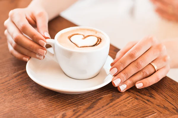 Mulher segurando xícara quente de café, com forma de coração — Fotografia de Stock