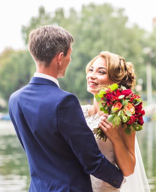 Onu açık havada kucaklayan Düğün çifti, sarılma bir buket çiçek, holding gelin damat