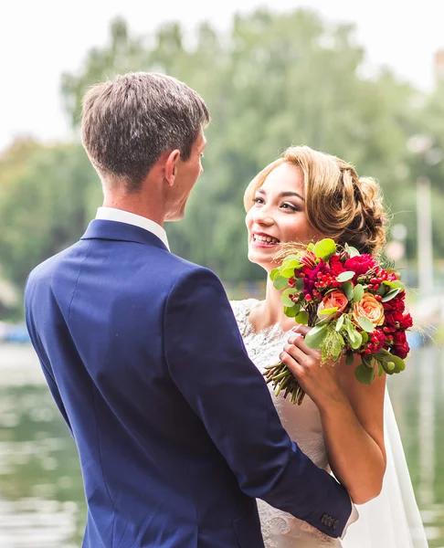 Onu açık havada kucaklayan Düğün çifti, sarılma bir buket çiçek, holding gelin damat