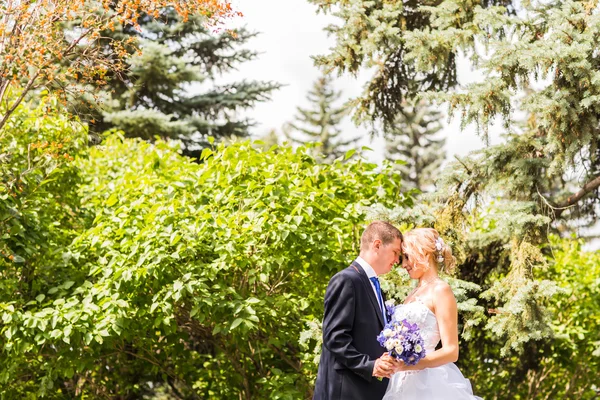 Casamento casal abraçando, a noiva segurando um buquê de flores, noivo abraçando-a ao ar livre — Fotografia de Stock