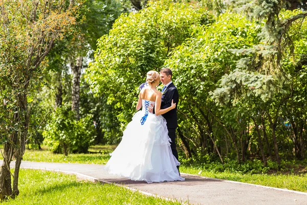 Pareja de boda abrazándose, la novia sosteniendo un ramo de flores, novio abrazándola al aire libre —  Fotos de Stock