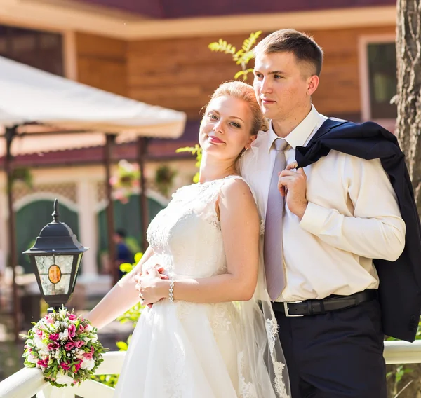 Wedding couple hugging, the bride holding a bouquet of flowers,  groom embracing her outdoors — Stock Photo, Image