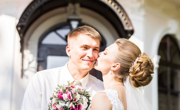 Bröllopsparet kramas, bruden håller en bukett blommor, groom omfamna henne utomhus — Stockfoto