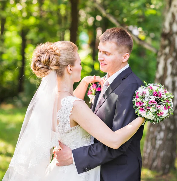 Bröllopsparet kramas, bruden håller en bukett blommor, groom omfamna henne utomhus — Stockfoto