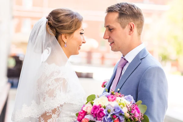 Couple de mariage câlin, la mariée tenant un bouquet de fleurs, marié embrassant son plein air — Photo