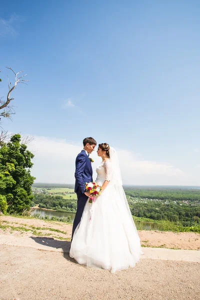 Bruidspaar knuffelen, het houden van een boeket bloemen, bruid bruidegom omarmen haar buitenshuis — Stockfoto