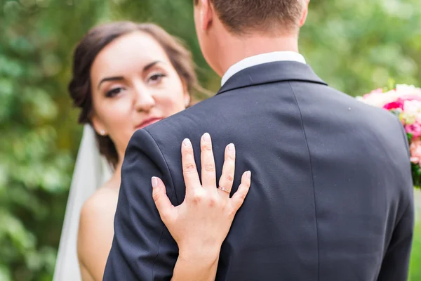 Pareja de boda abrazándose, la novia sosteniendo un ramo de flores, novio abrazándola al aire libre — Foto de Stock