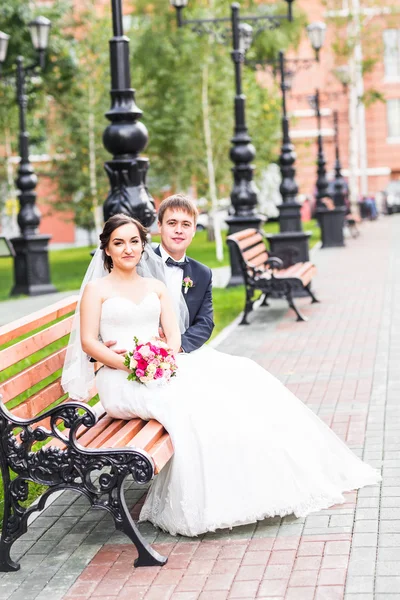 Couple de mariage câlin, la mariée tenant un bouquet de fleurs, marié embrassant son plein air — Photo