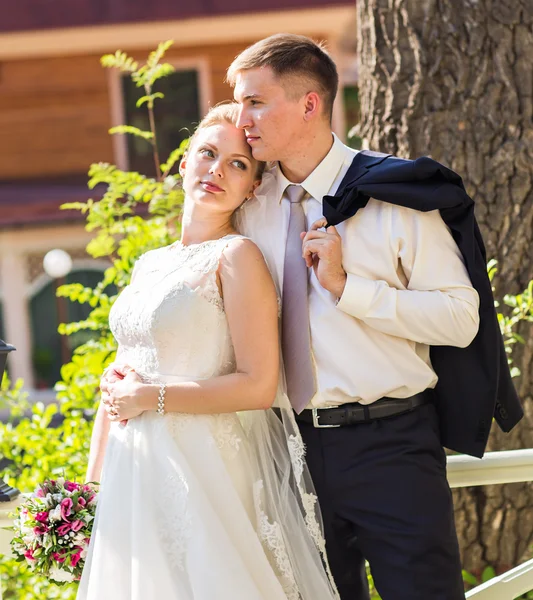 Wedding couple hugging, the bride holding a bouquet of flowers,  groom embracing her outdoors — Stock Photo, Image