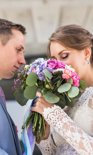 Bröllopsparet kramas, bruden håller en bukett blommor, groom omfamna henne utomhus — Stockfoto