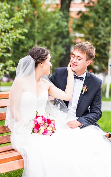 Couple de mariage câlin, la mariée tenant un bouquet de fleurs, marié embrassant son plein air — Photo