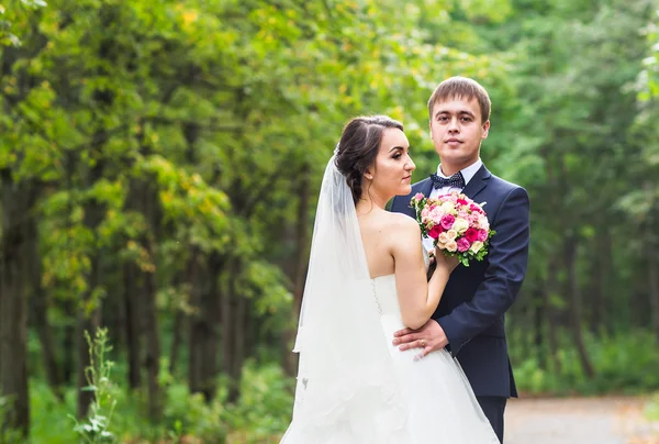 Novia y novio en el día de la boda caminando al aire libre. Recién casados felices abrazándose. Pareja amorosa . — Foto de Stock