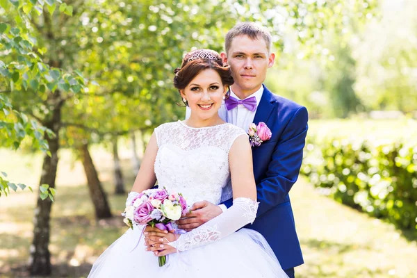 Wedding couple hugging, the bride holding a bouquet of flowers,  groom embracing her outdoors — Stock Photo, Image